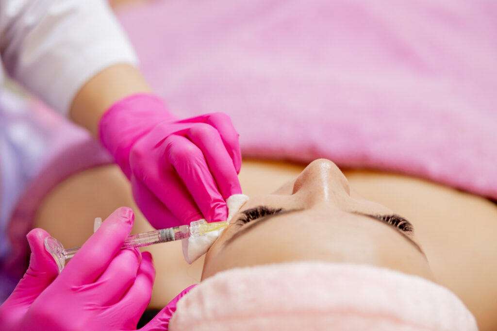 A provider wearing hot pink surgical gloves carefully administers the first injection in a patient's Dysport treatments in Tallahassee. The patient is laying on a treatment bed, relaxing as the injections are administered.