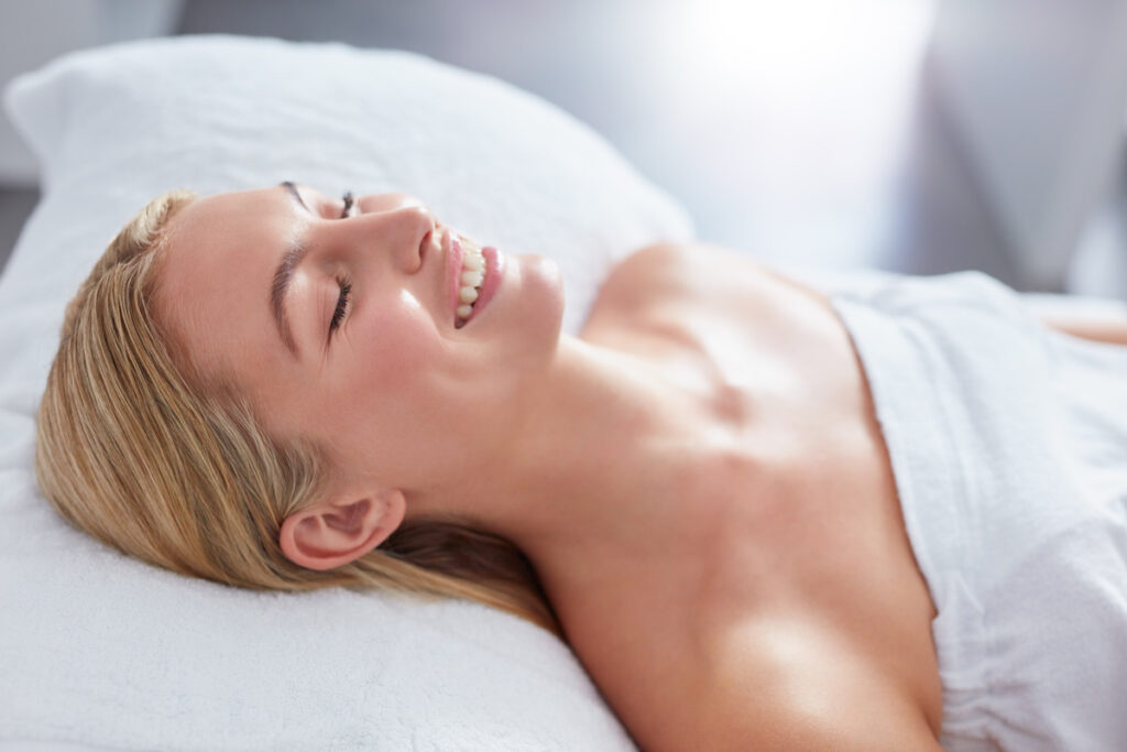 Close up shot of a woman in a day spa relaxing on a massage table and smiling. Caucasian woman wrapped in towel, ready for skin care in Thomasville, GA