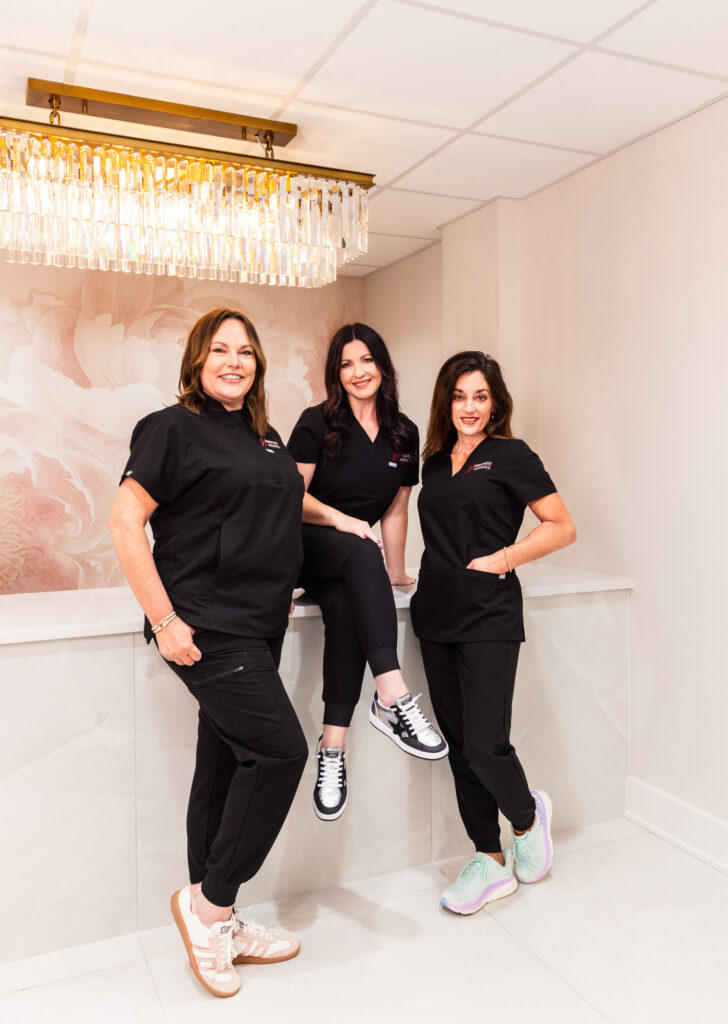 Our provider at Harmonized Aesthetics and her assistants, smiling. This is the team behind our facial contouring in Tallahassee, who have years of experience placing injectables.